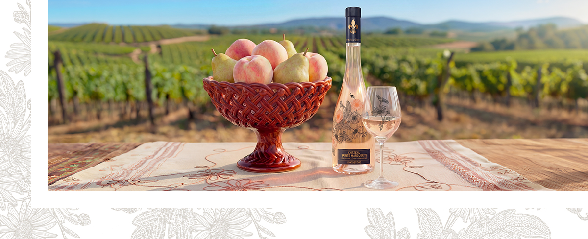 Bouteille de Château Sainte Marguerite Fantastique Rosé 202( sur une table en bois avec une coupe de fruits contenant des poires et des pêches, avec en fond un paysage de vignoble
