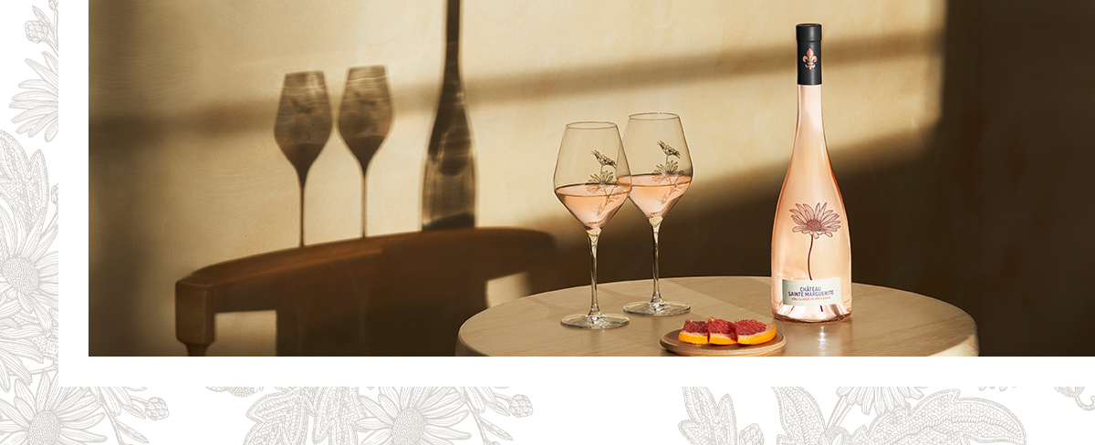 Cagette sur un vélo avec une bouteille de Château Sainte Marguerite Rosé 2025 dedans, sur un fond rouge ocre avec des ombres