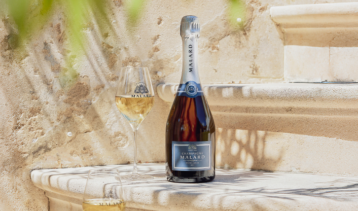Bouteille de Champagne Brut Excellence Malard sur des marches en extérieure de la propriété