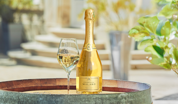Bouteille de Champagne Malard Blanc de Blancs Excellence sur un tonneaux de vin en extérieure de la propriété