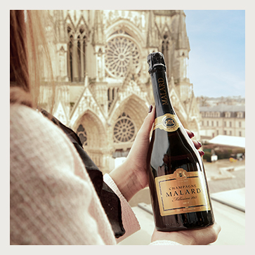 MILLÉSIMÉ 2015 EXCELLENCE tenue dans une main devant la Cathédrale Notre-Dame de Reims