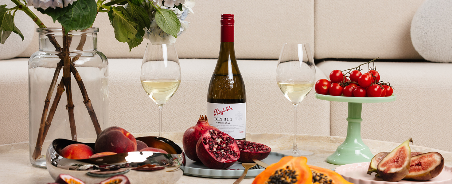 Bouteille de vin blanc Bin 311 Penfolds sur une table basse dans un salon, avec des fruits de grenade, de pêches et de papaye